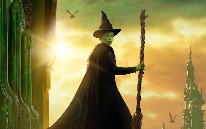 Elphaba in a pointed hat holding a broomstick.