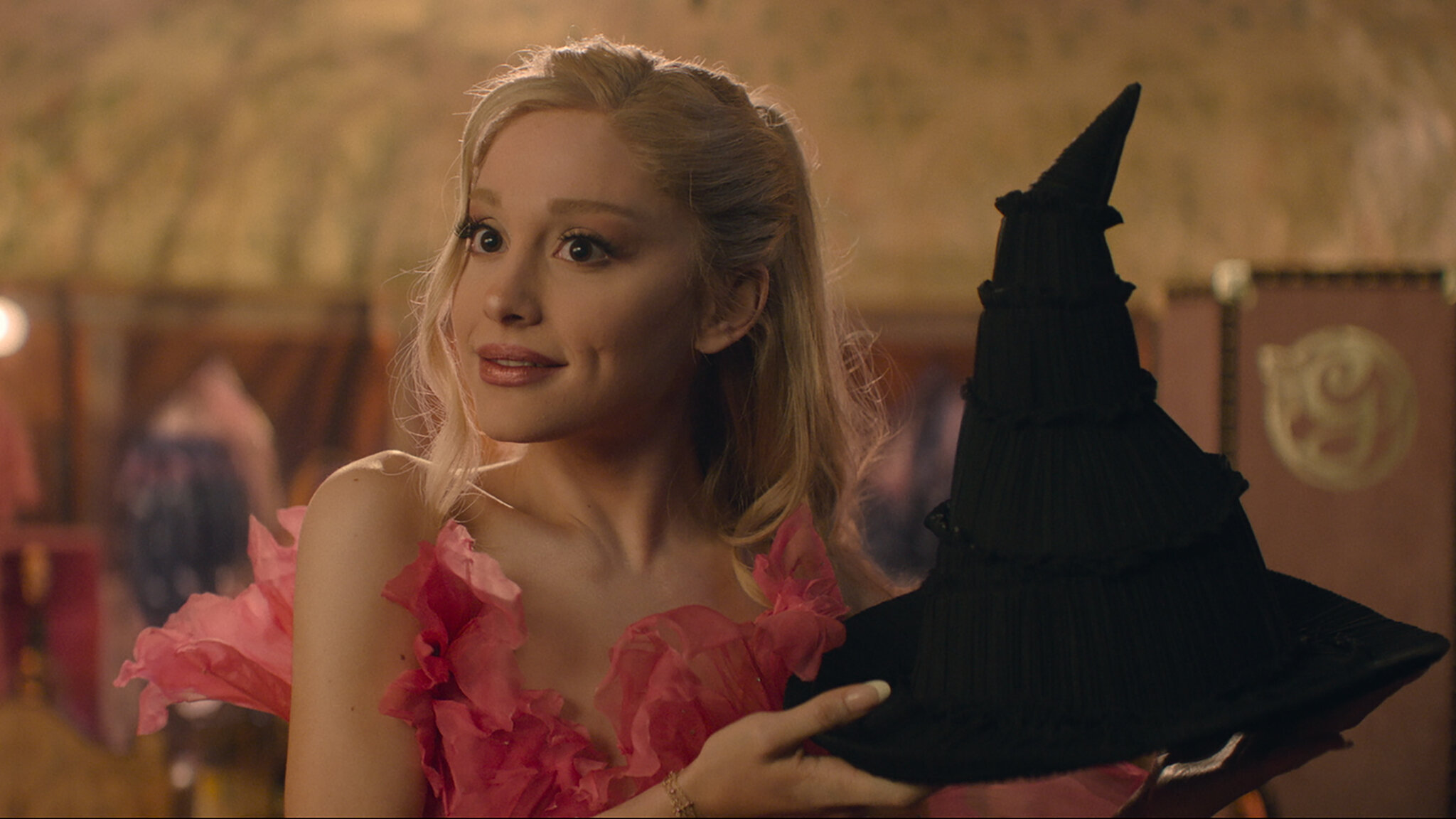 Glinda holding a black pointed witch hat.